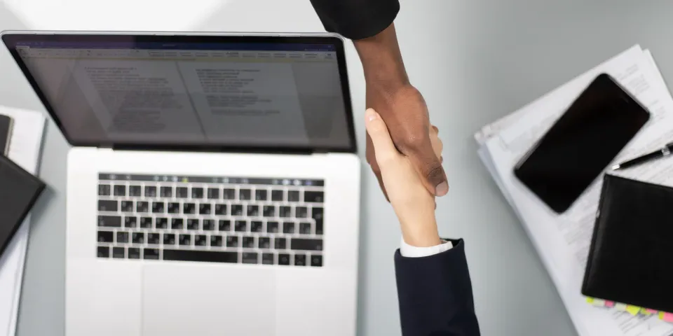 Zwei Geschäftspartner reichen sich über einem Laptop die Hand als Symbol für die Übergabe einer Microsoft-365-Umgebung beim IT-Dienstleisterwechsel