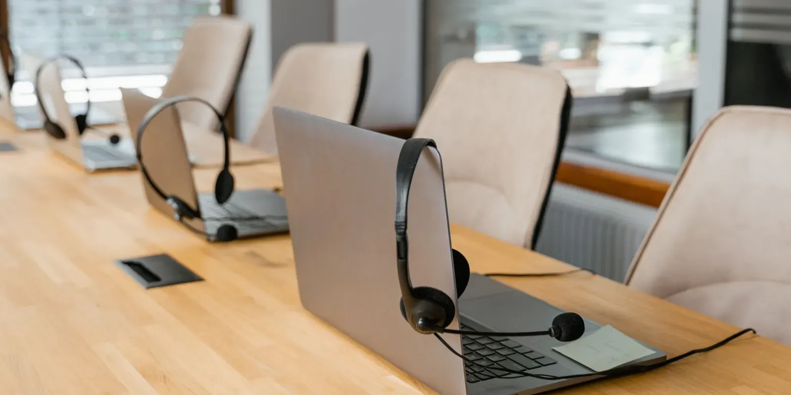 Mehrere Laptops mit Headsets an gleich ausgestatteten Arbeitsplätzen als Symbol für die Lizenzwahl je Arbeitsplatz